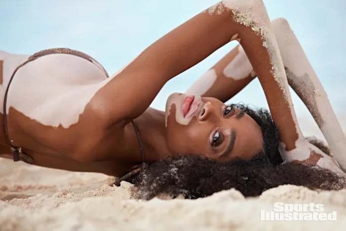Winnie Harlow lays on the sand wearing a string bikini.